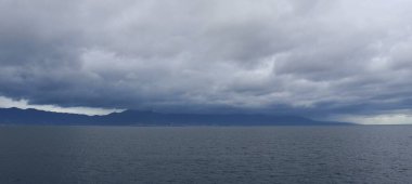 Denizde bulutlu bir gün ve adanın arka planında kara yağmur bulutları.