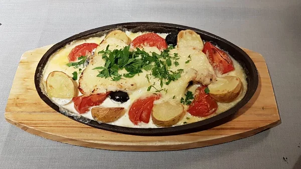 Carne al horno con papas y tomates en una sartén y servida en una tabla de madera —  Fotos de Stock