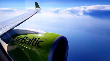 Kanat ve uçak motoru bulutların arka planındaki lombozdan geliyor. AirBaltic, Letonya, Temmuz 2019.