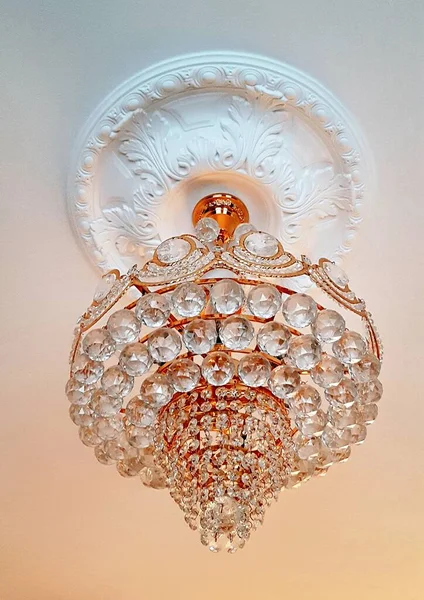 Beautiful chandelier with many round lenses is fixed in the center of the gypsum ornament — Fotografia de Stock