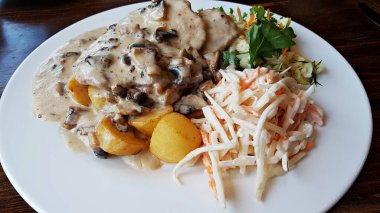 İki dilim mantar soslu pişirilmiş biftek, haşlanmış patates ve taze sebze salatası..