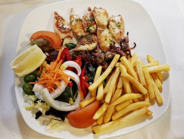 Kızarmış küçük kalamar dilimleri patates kızartması ve taze sebze salatası..