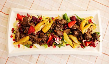 Taze sebzeli sığır güveci, böğürtlen ve büyük beyaz tabakta marul..