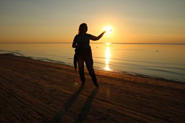 Denizde sakin bir havada, güzel bir günbatımının arka planında genç bir kadının silueti. 3 Haziran 2019. Letonya.