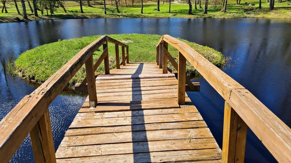 Small wooden bridge from the shore to small island in the lake on warm May day.