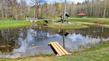 Small pond with a reflection on its surface of trees and an old well in early spring.
