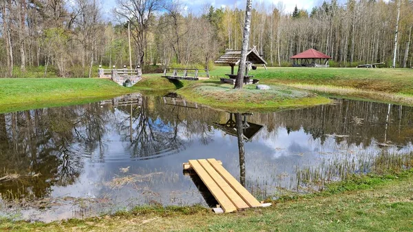 Small pond with a reflection on its surface of trees and an old well in early spring.