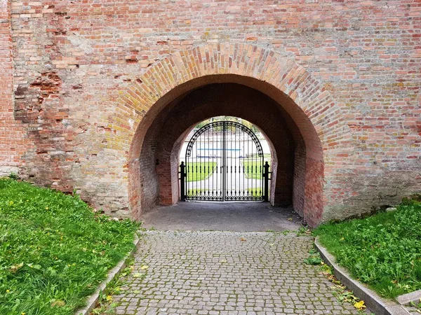An arch with metal gates in high wall built of red brick.