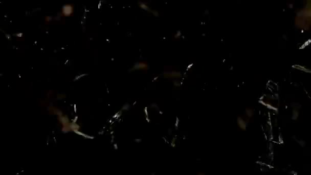 Fragments of broken glass fly in different directions on a black background. — Stockvideo