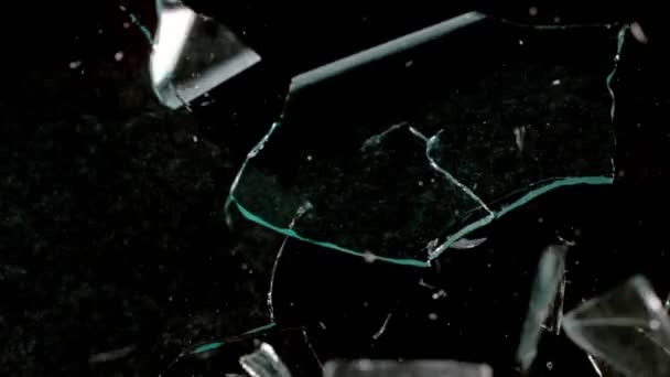 Fragmenty rozbitého skla létají různými směry na černém pozadí. — Stock video