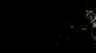 Kırık cam parçaları siyah arka planda farklı yönlere uçuyor..