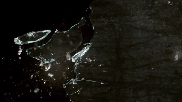 Fragmentos de vidro quebrado voam em direções diferentes em um fundo preto. — Vídeo de Stock