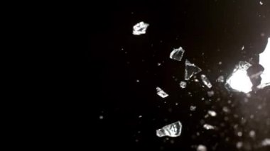 Kırık cam parçaları siyah arka planda farklı yönlere uçuyor..