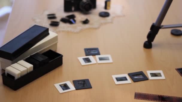 A vintage camera is lying on the table. Next to it is a 35 mm film cut into slides. — Stock videók