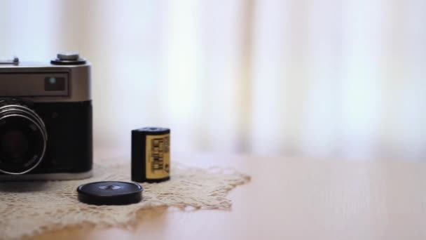 A vintage camera is lying on the table. Next to it is a 35 mm film cut into slides. — Video Stock
