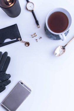 Beyaz tezgahın üstünde sade kahve olan beyaz bir kupa. Yakınlarda beyaz kremalar var. Bir telefon, siyah bir şapka ve siyah kadın aksesuarları. Üst görünüm.
