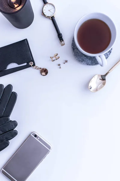 Uma caneca branca com café preto em uma bancada branca. Há merengues brancos nas proximidades. Um telefone, um chapéu preto e acessórios femininos pretos. Vista superior. — Fotografia de Stock