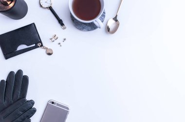 Beyaz tezgahın üstünde sade kahve olan beyaz bir kupa. Yakınlarda beyaz kremalar var. Bir telefon, siyah bir şapka ve siyah kadın aksesuarları. Üst görünüm.