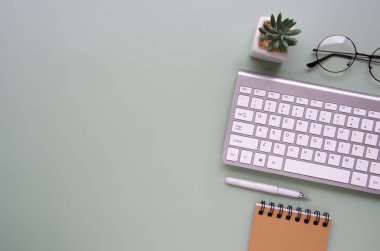 Bilgisayarlı ofis masası, yeşil çiçek, dosya. Not defteri, sosyal ağlar. Yukarıdan bak. Merkez ofis çalışma alanı. Aksesuarlar, yuvarlak gözlükler, yazmak için beyaz kalem, gri klavye