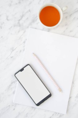 Masaüstü. Not defteri, telefon, kalem ve çay fincanı mermer arka planda. Üst görünüm