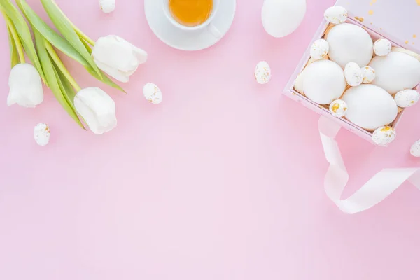 Laleli bir kutuda renkli yumurta manzarası bahar tatilinde bir fincan çay. Düz, pembe arkaplan