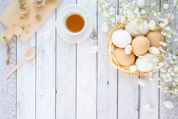 Mutlu Paskalya yumurtaları yuvada ve çiçek süslemeleri beyaz ahşap üzerinde