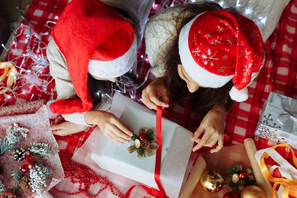 Noel şapkalı iki kız Noel hediyelerini paketliyor.
