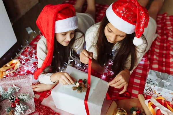 Noel şapkalı iki kız Noel hediyelerini paketliyor.