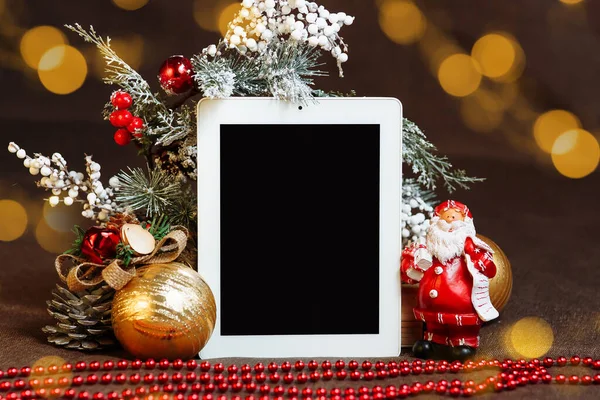 Noel süsleri arasında boş bir ekran bulunan dikey tablet ve Noel Baba maketi