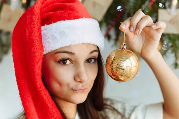 Noel şapkalı mutlu kız elinde Noel ağacı oyuncağıyla.