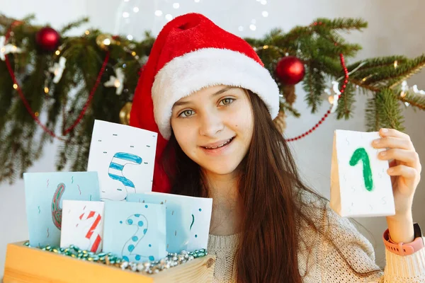 Noel şapkalı mutlu bir kız elinde Advent takvimi tutuyor.