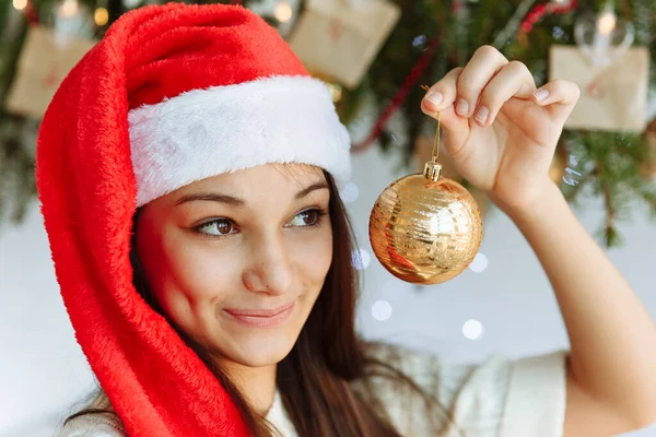 Noel şapkalı mutlu kız elinde Noel ağacı oyuncağıyla.