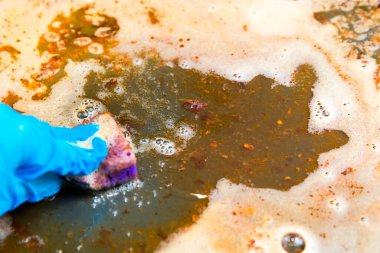 Eldivenli el, kirli yağlı çarşafı süngerle yıkar.