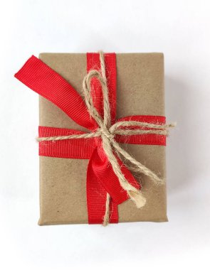 Üst görünüm, beyaz üzerine izole edilmiş kırmızı kurdele yayı ile el işi kağıdına sarılmış klasik hediye kutusu. Noel hediyesi.