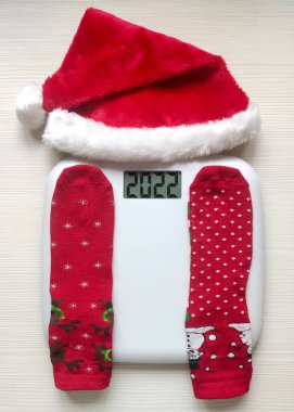Elektronik terazili Noel çorapları ve beyaz ahşap arka planda Noel Baba şapkası. Üst görünüm.