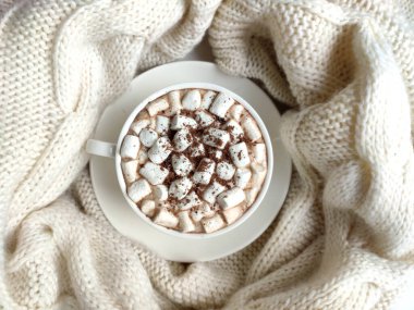 Örgü arka planda kremalı beyaz fincan sıcak kakao manzarası. Sıcak çikolatalı kış arkaplanı.