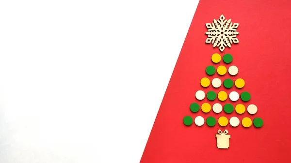 Çocuklardan yapılmış çok renkli Noel ağacı ahşap mozaik ve kırmızı arka planda ahşap kar tanesi. Dikey oryantasyon. Metin için boşluk.