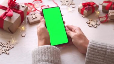 Noel arka planında dikey yeşil ekranlı, hediyeli akıllı telefonu olan bir kadın. Chroma Key 'li cep telefonu. Ellerini kapat..