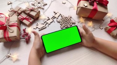 Noel arka planında yatay yeşil ekranlı ve hediyeli akıllı telefon tutan çocuk. Chroma Key 'li cep telefonu. Ellerini kapat..