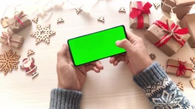 Noel arka planında dikey yeşil ekranlı ve hediyeli akıllı telefon tutan adam. Chroma Key 'li cep telefonu. Ellerini kapat..
