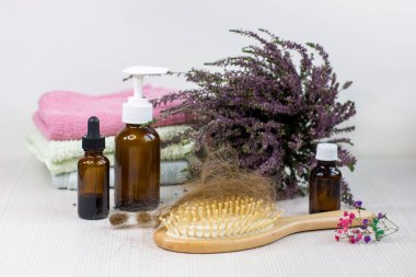 Medication bottles, hairbrush, towel and herb heather on white wooden table. A brush with lost hair on it. Concept of hair loss problem.