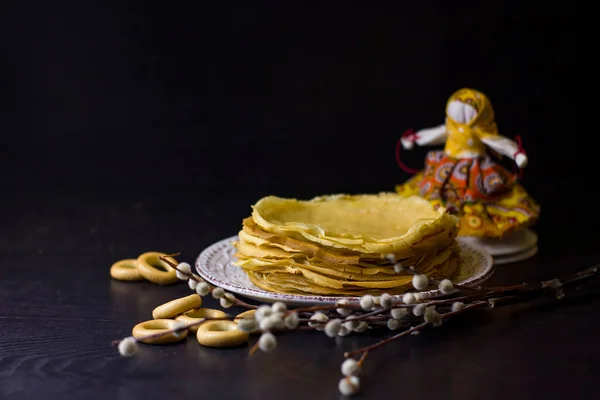 Background with pancakes, textile doll, sushki, and pussy-willow for Maslenitsa festival. Traditional Russian meal for Shrovetide. Greeting card or poster.Low key. Copy space.