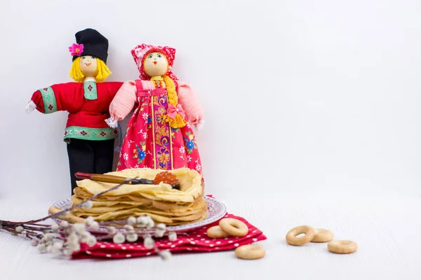 Background with pancakes, textile dolls, sushki, wooden spoon with caviar and pussy-willow on white for Maslenitsa festival. Traditional Russian meal for Shrovetide.Greeting card or poster.Copy space.