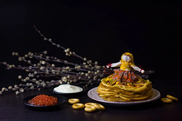 Background with pancakes, textile doll, sushki, caviar, sour cream and pussy-willow for Maslenitsa festival. Traditional Russian meal for Shrovetide. Greeting card or poster.Low key.