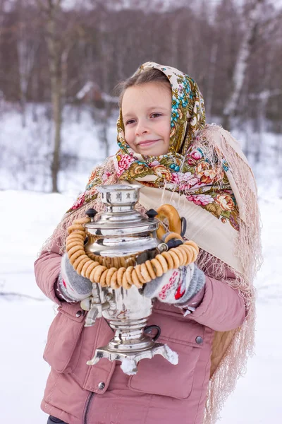 冬の背景にサモヴァールとベーグルを持つ伝統的なロシアのスカーフでかわいい女の子 マレニツァ祭 — ストック写真