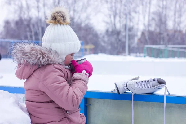かわいい女の子は屋外でスケートした後に暖かくなるために熱いお茶を飲んでいます — ストック写真