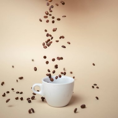 Beyaz kahve fincanının üzerine kahve çekirdeği dökmek. Açık kahverengi arkaplan.