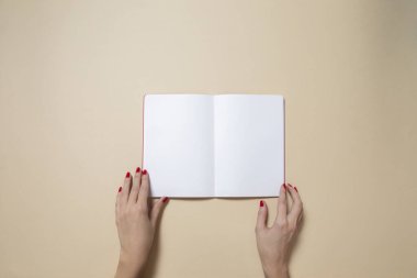 Açık bir defter ve açık kahverengi arka planda güzel kadın elleri.
