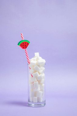 Bir bardak dolusu şeker ve mor arka planda bir pipet. Güzel fotoğraf, ferahlatıcı neşeli fikir. Şeker içeceği.