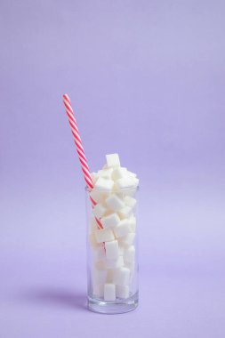 Bir bardak dolusu şeker ve mor arka planda bir pipet. Güzel fotoğraf, ferahlatıcı neşeli fikir. Şeker içeceği.
